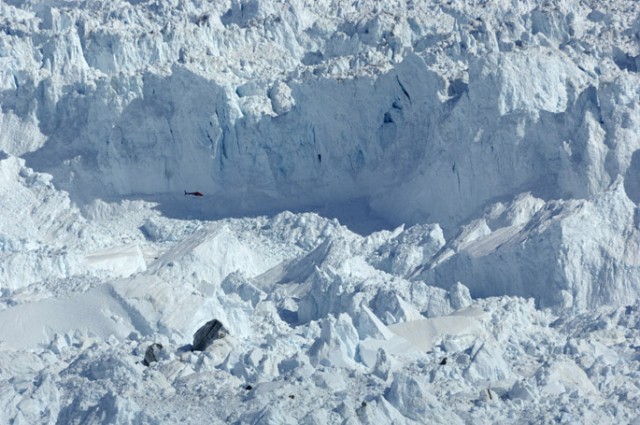 A helicopter flies past a section of the face of a glacier in Greenland.